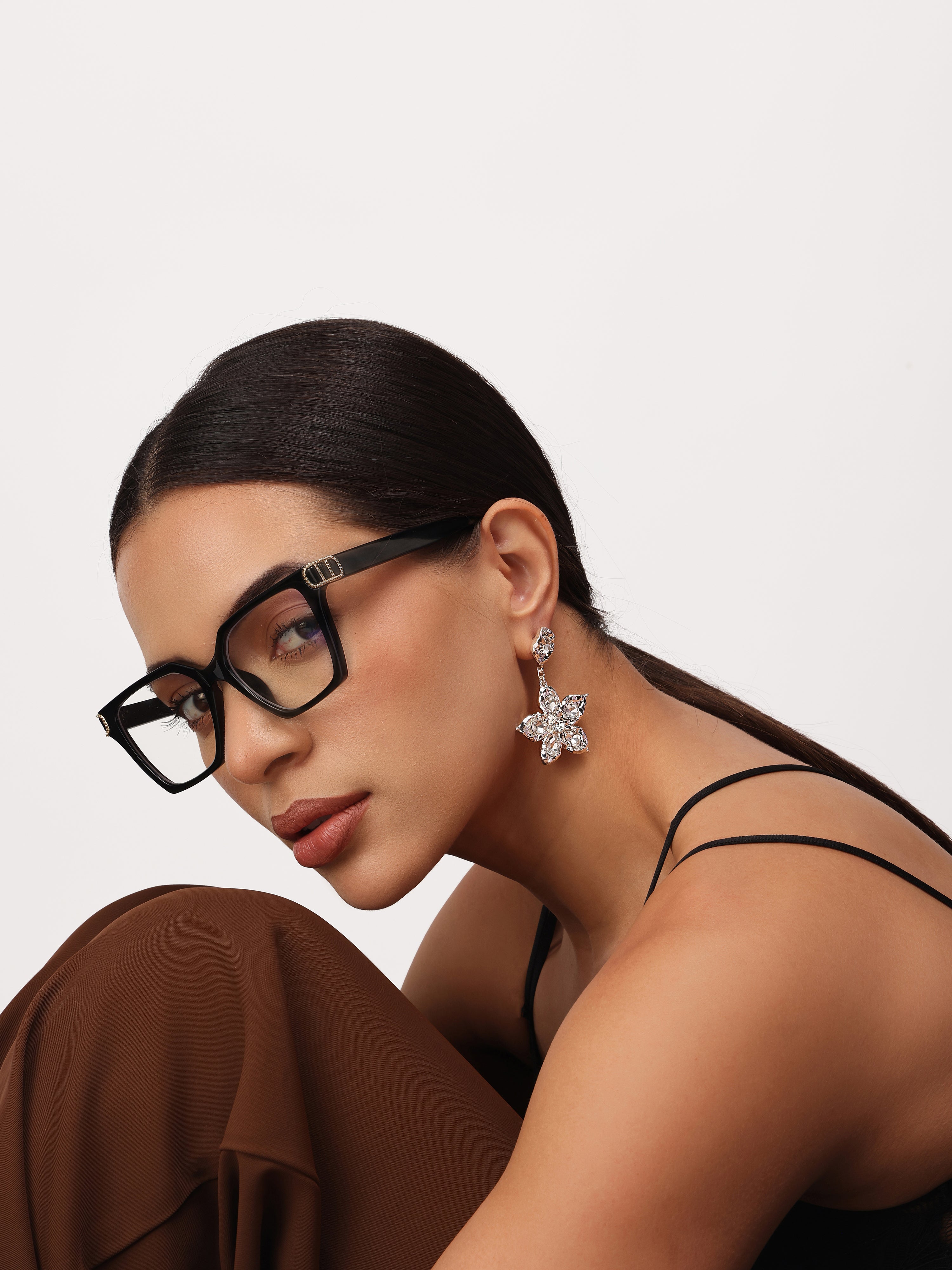 Woman wearing real gold plated flower shaped crystal stone drop earrings with a neutral background