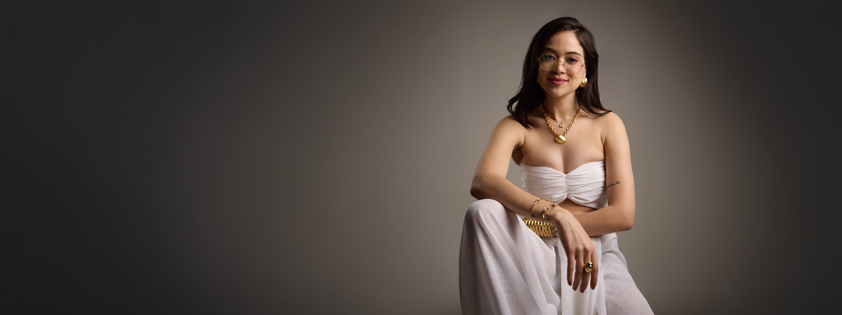 Woman in a strapless white dress sitting on a chair against a dark background
